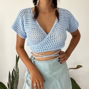 May include: A light blue crochet wrap top with a V-neck and short sleeves. The top is tied at the waist with matching strings.