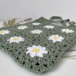 Peut inclure: Un sac en crochet vert avec des fleurs de marguerite blanches et jaunes.