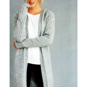 Könnte beinhalten: Eine Frau trägt einen hellgrauen, langen Rippstrick-Cardigan über einem weißen T-Shirt und einer schwarzen Hose. Der Cardigan hat eine Kapuze und reicht bis zur Mitte der Wade. Das Patons-Logo befindet sich oben rechts. Das Bild hat einen grauen Hintergrund.