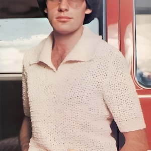 Könnte beinhalten: Ein Mann trägt ein weißes, gehäkeltes Kurzarmhemd mit Kragen. Er trägt eine goldgerahmte Sonnenbrille und hat kurze braune Haare. Er steht neben einem roten Auto.