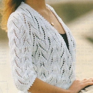 May include: A white crocheted cardigan with a V-neck and a button closure. The cardigan has a delicate lace pattern and three-quarter sleeves.