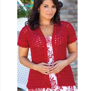 Może przedstawiać: Czerwony kardigan z szydełka z krótkimi rękawami. Kardigan z otwartym przodem jest noszony na białej sukience z czerwonym kwiatowym wzorem. Szydełkowy wzór ma otwarty, przewiewny ścieg. Kardigan jest w jednolitym, żywym czerwonym kolorze.