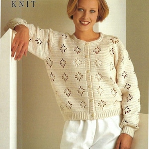 May include: A cream-colored crocheted cardigan with a button-up front and a floral pattern. The cardigan is shown on a model wearing white pants.