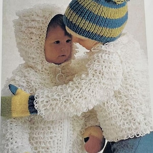 May include: Two children wearing white crocheted jackets with a zip closure. The child on the left is wearing a white crocheted hooded jacket with a yellow and blue striped mitten. The child on the right is wearing a blue and yellow striped knitted hat with a pom-pom.