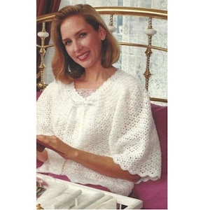 May include: A white crocheted top with a scalloped edge and a lace trim around the neckline. The top has a loose fit and is perfect for a casual, relaxed look.