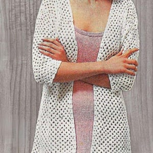 May include: White crochet cardigan with a loose fit and open front. The cardigan has a delicate, openwork pattern and is shown being worn over a pink tank top.