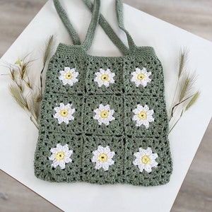 Peut inclure: Un sac cabas en crochet vert avec des fleurs de marguerite blanches et jaunes. Le sac a deux longues anses.