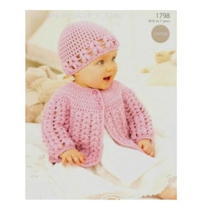 May include: A pink crocheted cardigan and hat set for a baby. The cardigan has a button fastening and the hat features a flower design.