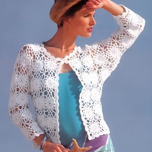 May include: A white crocheted cardigan with a delicate openwork pattern. The cardigan has a V-neck and long sleeves. The model is wearing a blue tank top underneath.