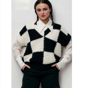 Puede incluir: Un chaleco de crochet a cuadros blanco y negro con cuello en V. El chaleco tiene mangas cortas y se lleva sobre una camisa blanca con cuello.