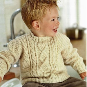 Op de afbeelding: Een crèmekleurige gebreide trui met een kabelbreipatroon. De trui heeft een ronde hals en lange mouwen.