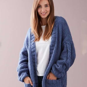 May include: A long, blue knitted cardigan with a V-neck and pockets. The cardigan is made of a soft, chunky yarn and has a relaxed fit.