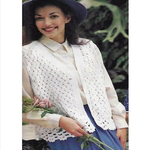 以下が含まれることがあります： レース模様の白いクロシェベスト。ベストはフロントオープンで、Vネックです。モデルは白いシャツと青いスカートを着用しています。