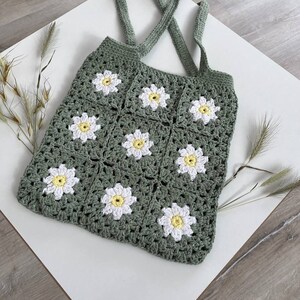 Peut inclure: Un sac cabas en crochet vert avec des fleurs de marguerite blanches et jaunes. Le sac a deux longues anses.