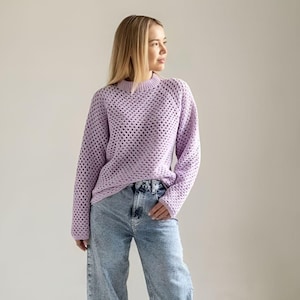 May include: A woman wearing a light purple open knit jumper and light blue jeans.