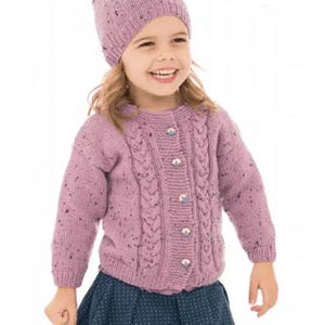 Op de afbeelding: Een gebreide lila hoed en vest set. Het vest heeft een kabelgebreid ontwerp aan de voorkant en is voorzien van knopen. De set is gemaakt van gespikkeld garen en wordt gecombineerd met een marineblauwe rok.