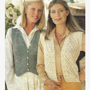 May include: Two women wearing knitted vests. The woman on the left is wearing a blue vest with buttons. The woman on the right is wearing a white vest with a lacy pattern.