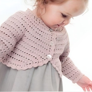 Op de afbeelding: Een lichtroze gehaakte trui met een gegolfde zoom en knoopsluiting. De trui is gemaakt van een delicaat, open steekpatroon.