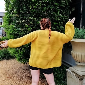 Peut inclure: Une femme portant un pull en maille jaune moutarde à manches longues et à texture côtelée. Elle porte un short noir et ses cheveux sont tressés.