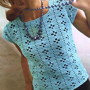 May include: A light blue crochet top with a delicate openwork pattern. The top has a square neckline and short sleeves.
