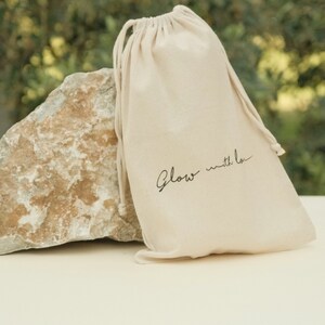 May include: A white drawstring bag with the text "Glow with Love" printed in black.