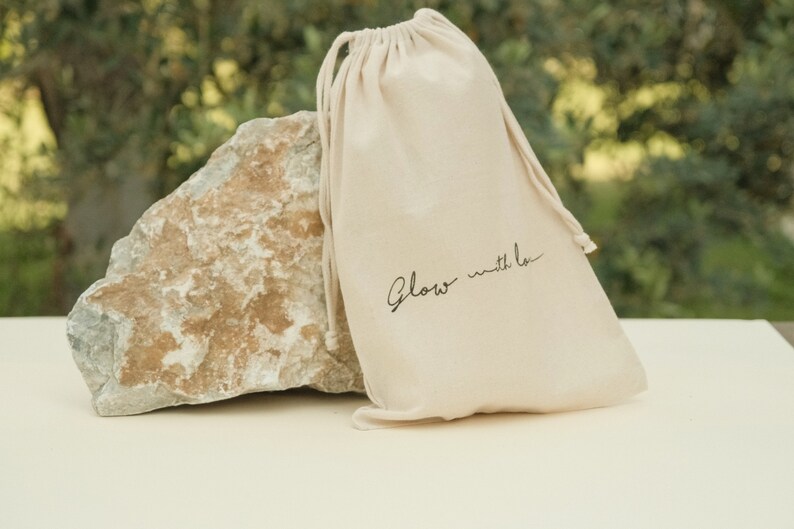 May include: A white drawstring bag with the text "Glow with Love" printed in black.
