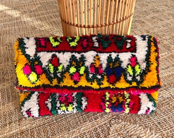 May include: A colorful woven clutch purse with a red, white, yellow, green, and blue floral pattern.