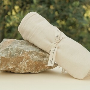 May include: A white cotton towel rolled up and tied with a ribbon that says "Glass with love". The towel is sitting on a gray rock.