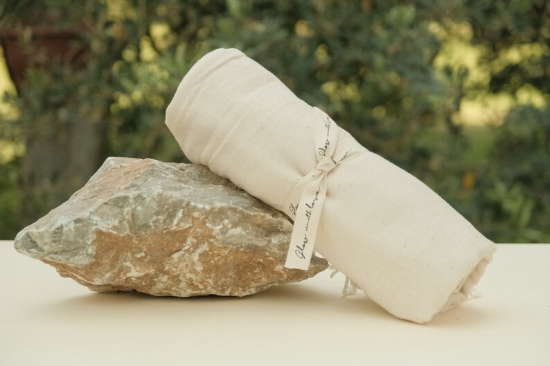 May include: A white cotton towel rolled up and tied with a ribbon that says "Glass with love". The towel is sitting on a gray rock.