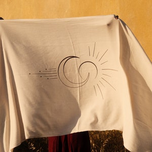 May include: A white cotton throw blanket with a black and white sun and moon design. The blanket has fringe on the edges.