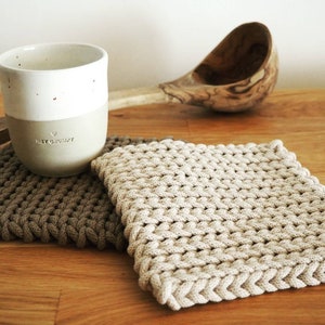 Könnte beinhalten: Zwei gehäkelte Topflappen, einer braun und einer beige, mit einer weißen Keramiktasse mit dem Text "Hey Grumpy" auf einer Holzoberfläche.