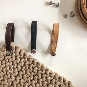 Könnte beinhalten: Drei verschiedene Ledergriffe mit Metallnieten. Die Griffe sind braun, schwarz und beige. Die Griffe befinden sich auf einem weißen Hintergrund.