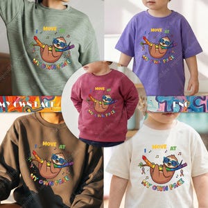 Op de afbeelding: Verschillende shirts en sweatshirts met een cartoon luiaard met een zonnebril en hangend aan een tak. De tekst "I MOVE AT MY OWN PACE" staat in kleurrijke letters boven en onder de luiaard. De kledingstukken zijn in verschillende kleuren.