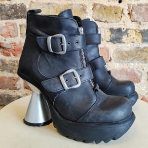 May include: Black leather ankle boots with silver buckles and a chunky platform heel. The heel is shaped like a cone.