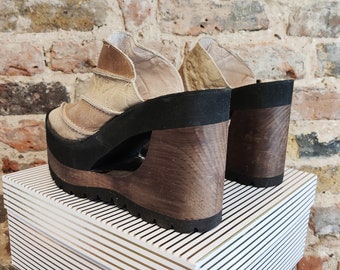 Könnte beinhalten: Ein Paar braune Plateau-Keil-Sandalen mit einem Holzabsatz. Die Sandalen haben ein Obermaterial aus abgenutztem Leder und eine schwarze Gummisohle.