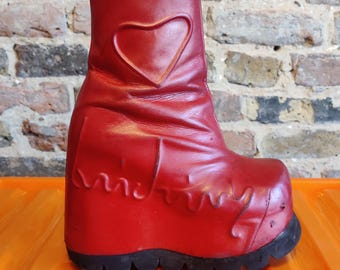Könnte beinhalten: Ein roter Plateau-Stiefel mit einem herzförmigen Ausschnitt an der Seite. Der Stiefel hat eine klobige Sohle und ein dekoratives Wellenmuster auf der Vorderseite. Der Stiefel ist aus glattem, glänzendem Material.
