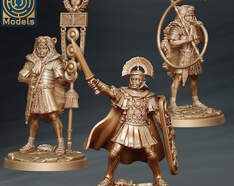 May include: Three miniature figures of Roman soldiers, painted in a gold metallic finish. The figures are posed in different stances, one holding a shield, one holding a horn, and one holding a staff with a decorative top. The figures are standing on circular bases.