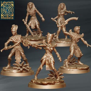 May include: A collection of five bronze-colored Egyptian-themed figurines. Each figure is posed in an action stance and is adorned with detailed pharaonic attire, including headdresses, armor, and weapons. The figures are set on small, textured bases with minimal foliage.