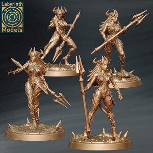 May include: Four gold-coloured miniature figures of female demons with horns and tails, each holding a spear-like weapon. The figures are standing on circular bases with a textured surface.
