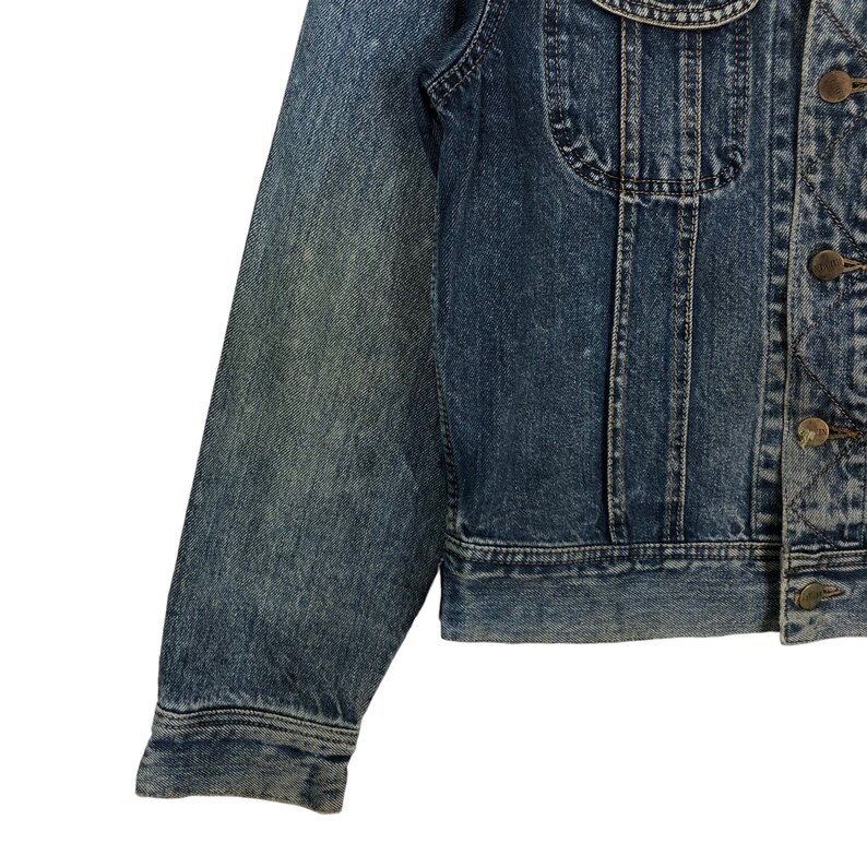 Puede incluir: Una chaqueta vaquera azul con cierre de botones y mangas largas. La chaqueta tiene un aspecto descolorido y est&aacute; hecha de un material suave y c&oacute;modo.