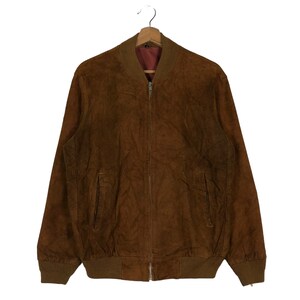 May include: A brown suede bomber jacket with a full-length zipper closure, ribbed cuffs, and a ribbed collar. The jacket has two front pockets and is hanging on a wooden hanger. The interior lining is a darker shade of brown.