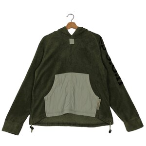 Könnte beinhalten: Olivgrüner Kapuzenpullover mit hellgrüner Tasche und Kordelzug. Auf dem Ärmel steht das Wort "SPORTING" in Schwarz. Der Pullover ist aus einem weichen, strukturierten Material gefertigt.