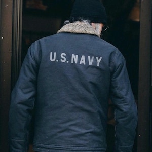 May include: A dark blue denim jacket with a faux fur collar and the text "U.S. NAVY" on the back.