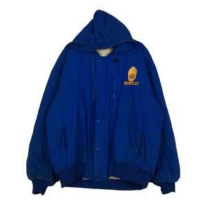 Könnte beinhalten: Blaue Kapuzenjacke mit Druckknopfverschluss. Auf der Brust befindet sich ein gold-blaues Emblem mit der Aufschrift "Cal Berkeley". Die Jacke hat einen gerippten Saum und Bündchen sowie zwei Vordertaschen.