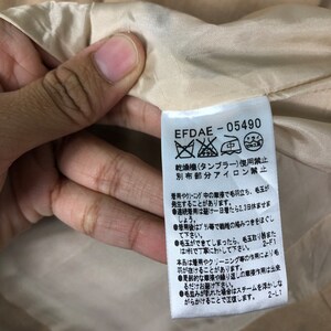 Op de afbeelding: Close-up van een label met de tekst "EFDAE-05490" en Japanse karakters. Het label is wit met zwarte tekst en is bevestigd aan een beige stof. Het label geeft onderhoudsinstructies.