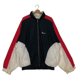 May include: A vintage Nike track jacket in black, red, and white. The jacket features a full zip, a white Nike swoosh logo on the chest, and a ribbed hem and cuffs. The sleeves are red, and the body is black and white.