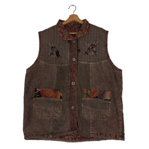 May include: Brown corduroy vest with embroidered golf club designs. Features a patterned collar and pocket accents. The vest has a button-up front and two front pockets. The vest is hanging on a wooden hanger.