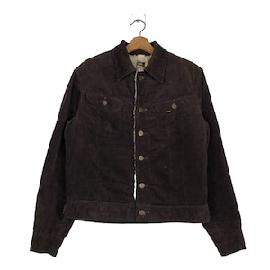 May include: A brown corduroy jacket with a button-up front, two chest pockets, and two side pockets. The jacket has a light-colored lining and a collar. The Lee logo is visible on the chest pocket. The jacket is hanging on a wooden hanger.