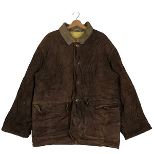 May include: A brown corduroy jacket with a contrasting green collar and two large front pockets. The jacket has a button-up closure and is hanging on a wooden hanger. The jacket appears to be vintage or pre-owned.