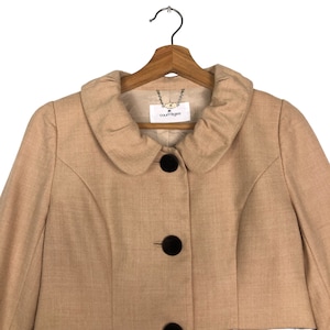 Op de afbeelding: Een beige jasje met een ronde kraag en drie grote, donkerbruine knopen. De jas hangt aan een houten kleerhanger. Het label luidt "courreges".